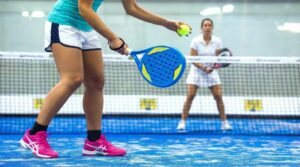 Padel player performing underarm serve on enclosed court